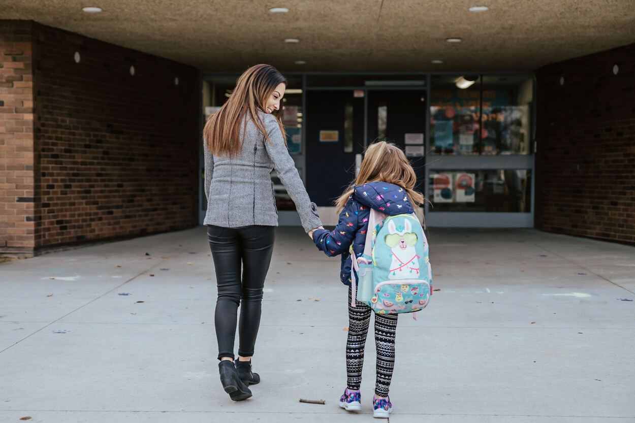 Mom holding hand of child walking towards school building