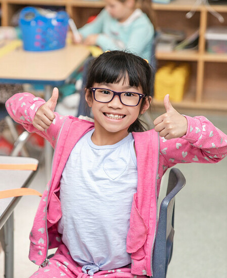 Young student sitting at table smiling with her thumbs up