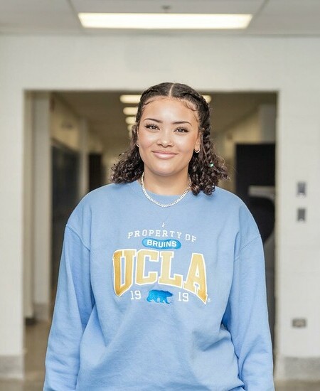 Female student wearing UCLA sweater standing in hallway with lockers